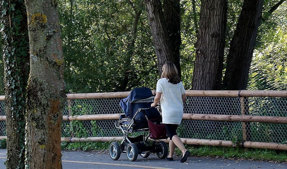 Mujer que pasea un bebé en su carrito por el parque